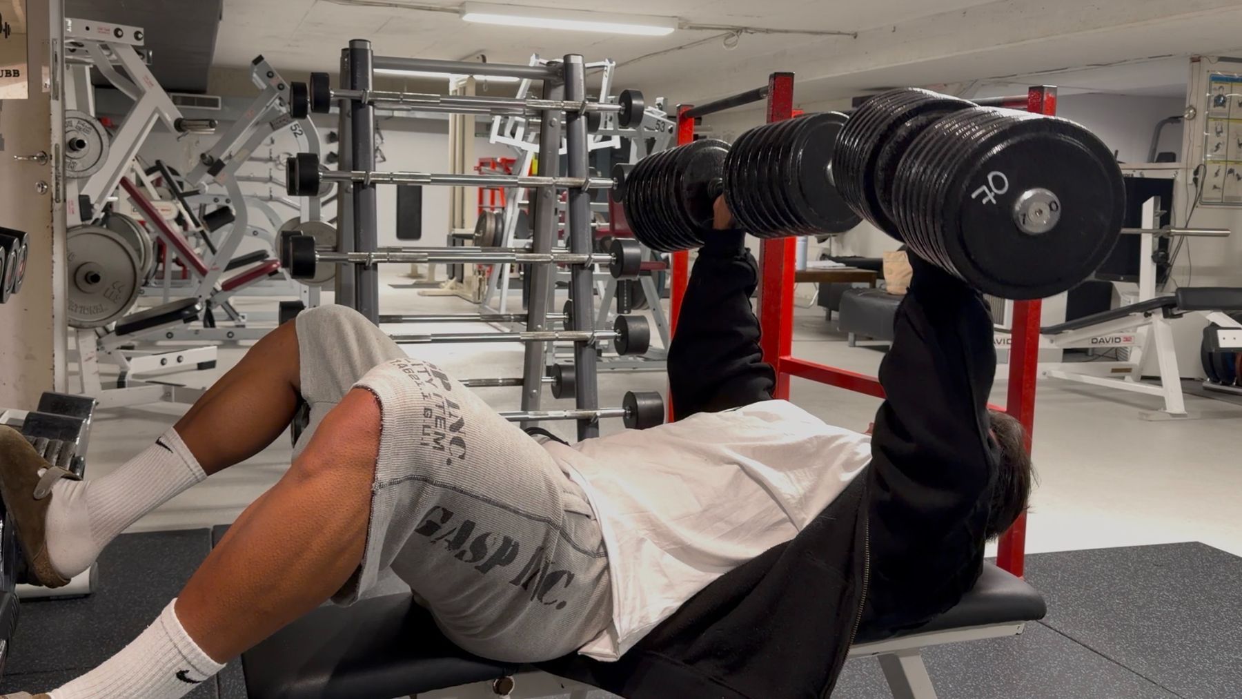 Coachen tar benkpress med tunge manualer i treningsstudioet